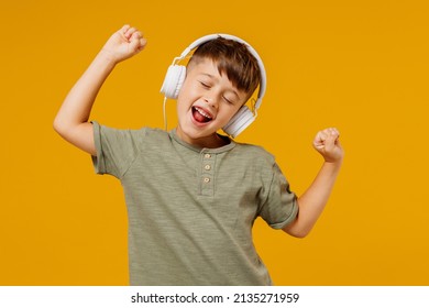 Little Small Cheerful Happy Boy 6-7 Years Old Wearing Green T-shirt Headphones Listen To Music Dance Isolated On Plain Yellow Background Studio Portrait. Mother's Day Love Family Lifestyle Concept.