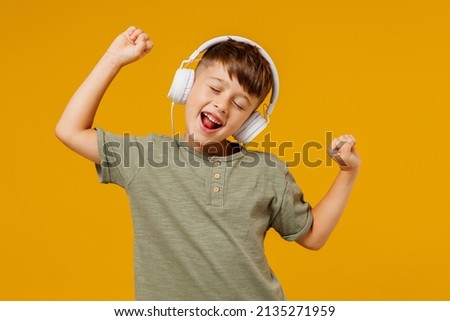 Little small cheerful happy boy 6-7 years old wearing green t-shirt headphones listen to music dance isolated on plain yellow background studio portrait. Mother's Day love family lifestyle concept.