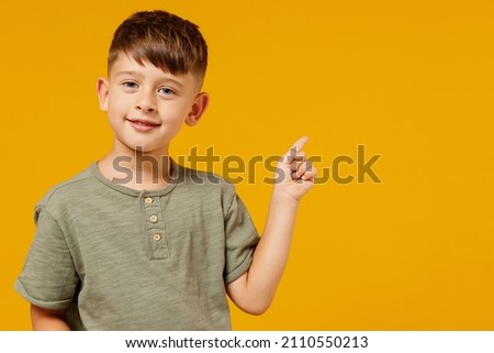 Little small happy boy 6-7 years old in green casual t-shirt point index finger aside on workspace area isolated on plain yellow background studio portrait. Mother's Day love family lifestyle concept.