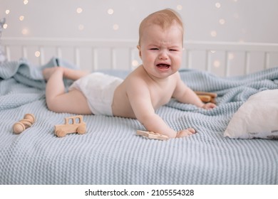a little small sad crying 6 months old baby infant boy in a diaper laying on the bed trying to crawl, crying. Teething and baby's illnesses problems, Bad mood, hungry baby