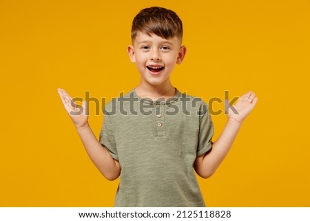 Little small smiling amazed happy boy 6-7 years old wearing green casual t-shirt look camera spread hands isolated on plain yellow background studio portrait Mother's Day love family lifestyle concept