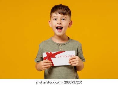 Little small smiling happy boy 6-7 years old wearing green t-shirt hold gift certificate coupon voucher card for store isolated on plain yellow background. Mother's Day love family lifestyle concept