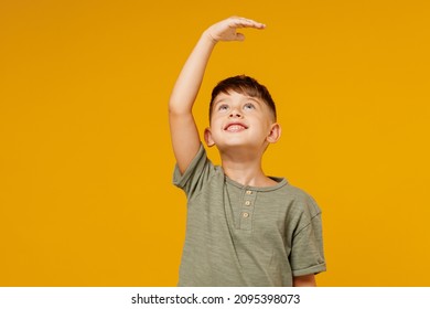 Little small smiling happy boy 6-7 years old wearing green casual t-shirt want to grow up, show height isolated on plain yellow background studio portrait. Mother's Day love family lifestyle concept
