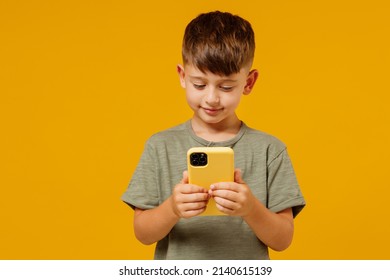 Little Small Smiling Happy Boy 6-7 Years Old Wearing Green T-shirt Hold In Hand Use Mobile Cell Phone Isolated On Plain Yellow Background Studio Portrait. Mother's Day Love Family Lifestyle Concept