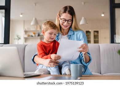 Little small toddler kid child son helping her busy young mother with freelance remote work holding papers, documents and domestic bills at home on lockdown during maternity leave - Powered by Shutterstock