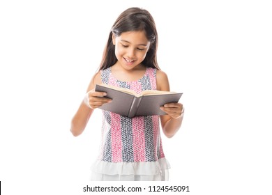 Little smart girl holding a book and reading it while standing against white background
