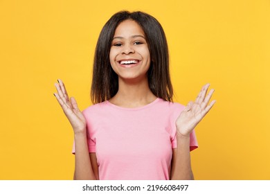 Little Smiling Amazed Kid Girl Of African American Ethnicity 12-13 Years Old In Pink T-shirt Look Camera Spread Hands Isolated On Plain Yellow Background Studio Portrait. Childhood Lifestyle Concept