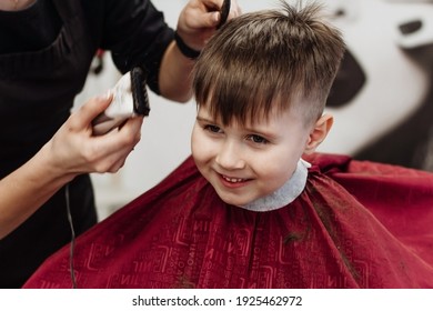 Little Smiling Boy Cut With Hairdresser's Machine. Close-up Of Woman Hands Grooming Kid Boy Hair In Barber Shop. Portrait Of Male Child At The Barber Shop To Cut His Hair.