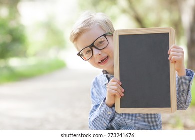 little smiling boy in cute glasses holding empty chalkboard, back to school concept - Powered by Shutterstock