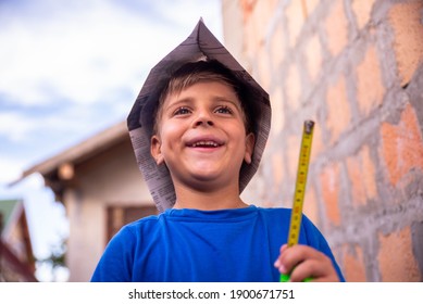 A Little Smiling Boy With A Newspaper Hat Holds A Measuring Tape In His Hands