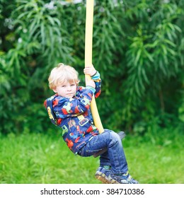 Little smiling boy of three years having fun on swing on sunny summer day, outdoors. Active sports with kids.