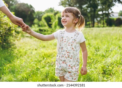 Little smiling cheerful fun happy kid girl 5-6 years old wear white casual clothes hold hand walk with mother on park green lawn, spend time outdoor in village countyside during summer time vacations - Shutterstock ID 2144392181