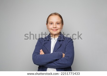 Little smiling cute pretty clever kid child girl 10 year old wearing blue school uniform standing with crossed arms on grey background