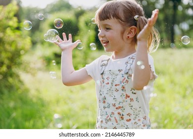 Little smiling excited happy kid girl 5-6 years old in white casual clothes blowing bubbles play on park green sunshine lawn, spending time outdoor in village countyside during summer time vacations - Shutterstock ID 2146445789