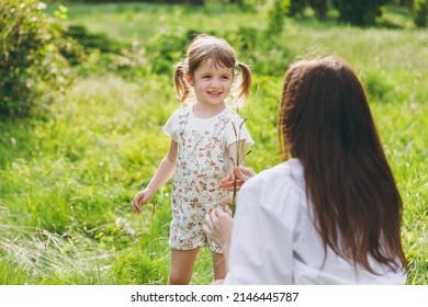 Little smiling fun happy kid girl 5-6 years old in white casual summer clothes gift flower grass to mother on park green lawn, spend time outdoor in village countyside during summer time vacations. - Shutterstock ID 2146445787