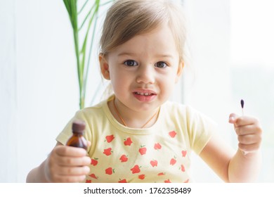 Little Smiling Girl Holding A Medicine Jar Of Iodine And An Ear Stick In Her Hands. Treatment Of Rashes, Acne, Pimples Dermatic Diseases, Contagious Mollusks On Skin In Children. Copy Space.