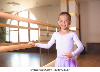 a little smiling girl in pointe shoes does stretching in ballet class near a frame and a big mirror - Shutterstock ID 2089736137