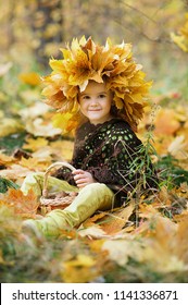 Little smiling girl sitting on a plaid in an autumn park. Cute Caucasian girl in autumn park holding yellow maple leaf in hand. kid in head wreaths