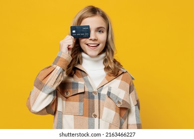 Little smiling happy cheerful blonde caucasian kid girl 13-14 years wearing checkered shirt hold cover eye with credit bank card isolated on plain yellow background studio. People lifestyle concept - Shutterstock ID 2163466227