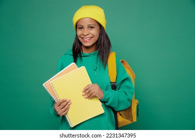 Little smiling happy fun kid teen girl of African American ethnicity 13-14 years old wear casual hoody hat backpack hold notebooks isolated on plain dark green background Childhood education concept - Shutterstock ID 2231347395