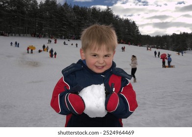 Little smiling proud blond boy in winter clothes with winter gloves on his hands holding a big snow globe - Powered by Shutterstock