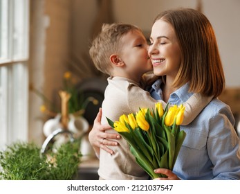 Little son congratulating mom with Mothers day at home, kisses her and giving her fresh flower bouquet, happy   woman mother embracing son. Family holidays and celebration concept - Shutterstock ID 2121037547