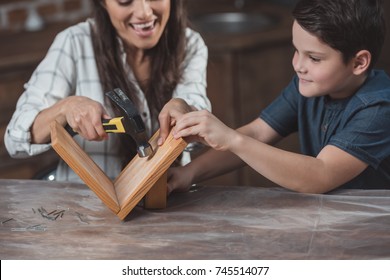 Little Son And His Mother Crafting A Wooden Birdhouse With Hammer