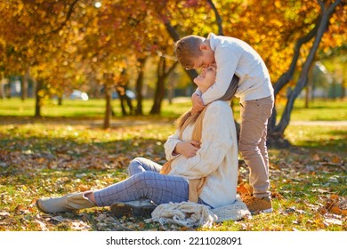 Little Son Hugs His Pregnant Mom On The Nature. Boy And Smiling Pregnant Woman Sitting In Autumn Park. Young Happy Family Waiting Baby. Pregnant Woman Enjoying Time With Her Child