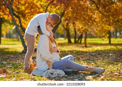 Little Son Hugs His Pregnant Mom On The Nature. Boy And Smiling Pregnant Woman Sitting In Autumn Park. Young Happy Family Waiting Baby. Pregnant Woman Enjoying Time With Her Child