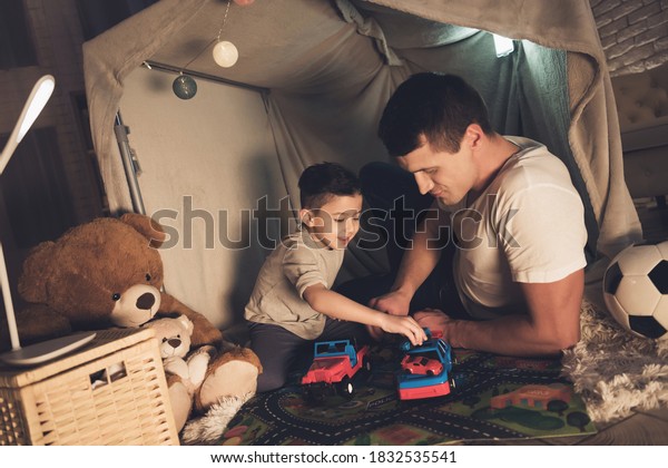 Little son\
plays in cars with dad in a toy house. Cheerful dad lies with his\
son in the house and plays toys at night.\
