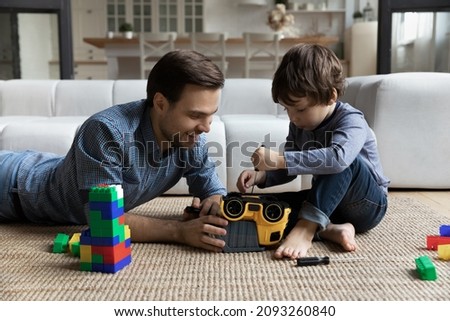 Little son repairing toy car with loving young father, using screwdriver, sitting playing on warm floor in living room, happy dad and adorable child boy having fun, spending leisure time together
