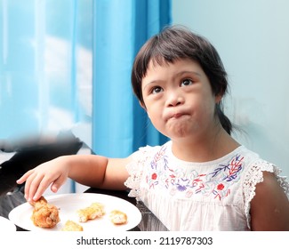 Little South East Asian Girl Eating Lunch Sitting At Dining Table. She Have Down Syndrome