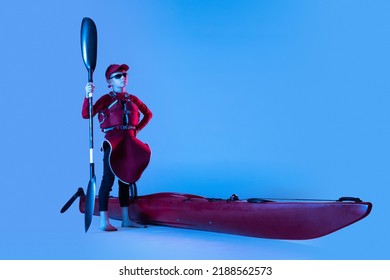 Little sportsman. Beginner kayaker in red canoe, kayak with a life vest and a paddle isolated on blue background in neon. Concept of sport, nature, travel, active lifestyle. Copy space for ad, design