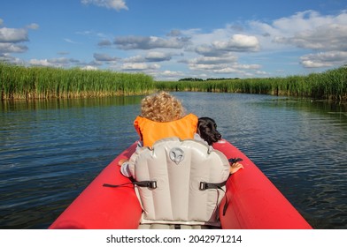 A Little Sporty Girl In A Life Jacket Floats On The Zdwyzh River On A Red Kayak With A Black Dog Cocker Spaniel. Ukraine