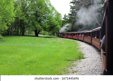 A Little Steam Train With Puff Of Smoke From Smoke Stack Running Across The Green Lawn 