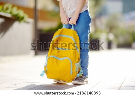 Little student with a backpack near school building. Close-up of child legs, hands and schoolbag of boy standing on staircase of schoolhouse. Kids back to school concept.