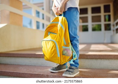 Estudiante pequeño con una mochila en las escaleras del edificio de la escuela. Cierre de las piernas, manos y bolso de niño parado en la escalera de la escuela. Los niños vuelven al concepto escolar.