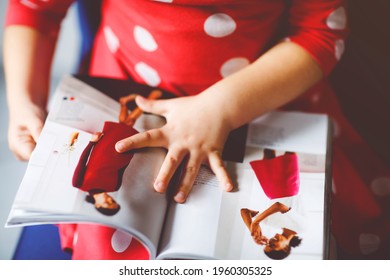 Little Stylish Toddler Girl Reading And Looking Fashion Magazine Or Catalogue. Adorable Child Having Fun With Choosing Clothes.