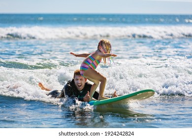 Little Surf Girl - Young Surfer Learn To Ride On Surfboard With Instructor At Surfing School. Active Family Lifestyle, Kids Water Sport Lessons, Swimming Activity In Summer Camp. Vacation With Child.