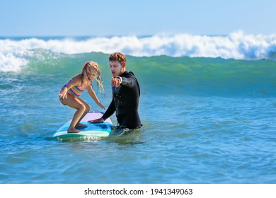 Little Surf Girl - Young Surfer Learn To Ride On Surfboard With Instructor At Surfing School. Active Family Lifestyle, Kids Water Sport Lessons, Swimming Activity In Summer Camp. Vacation With Child.