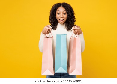 Little surprised happy kid teen girl wearing white casual clothes hold open look at paper package bags after shopping isolated on plain yellow background. Black Friday sale buy day lifestyle concept - Powered by Shutterstock