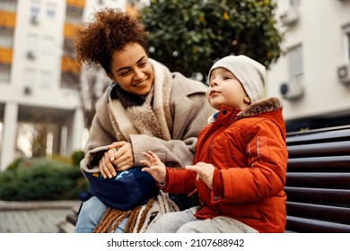 Little Talkative Boy Sitting With His Nanny Of Caregiver On The Bench Outside And Telling A Story.