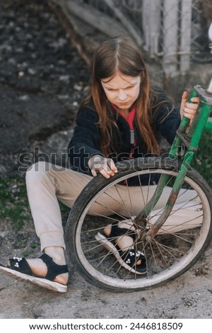 Little teenage girl, dissatisfied, distressed child sits near an old bicycle with a broken, punctured wheel tire outdoors. Photography, portrait.