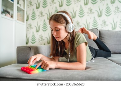 A little teenage girl is lying on the couch listening to music and relaxing with the help of a pop it toy - Powered by Shutterstock