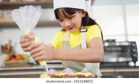 Little toddler asian girl child in apron and chef hat whipped cream decorating preparing homemade cupcakes in home kitchen. A Little girl preparing and decorating homemade cake. Children cooking - Powered by Shutterstock