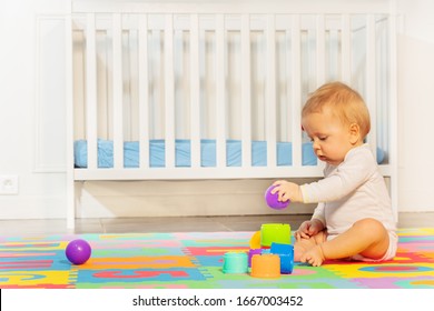 Little Toddler Baby Boy Sit In The Room On Children Carpet Near Crib Build Pyramid Of Blocks