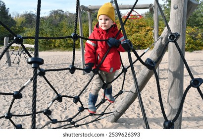 Little toddler boy climbing rope net on the playground in the public park. - Powered by Shutterstock