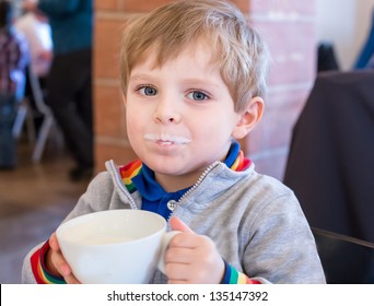 Little Toddler Boy Drinking Cup Of Milk In Restaurant