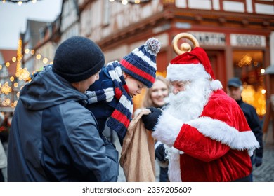 Little toddler boy with father on Christmas market. Happy kid taking gift from Santa Claus. Smiling man and son, family celebrating traditional holiday - Powered by Shutterstock