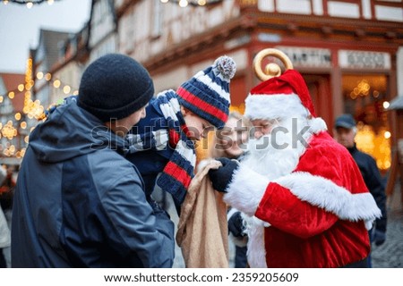 Little toddler boy with father on Christmas market. Happy kid taking gift from Santa Claus. Smiling man and son, family celebrating traditional holiday